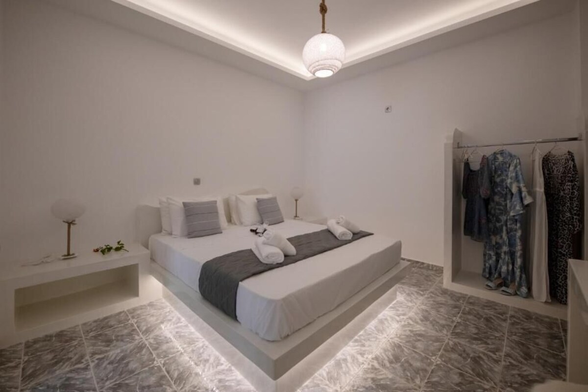 A modern bedroom with a bed, bedside tables, a hanging light fixture, and a clothing rack.