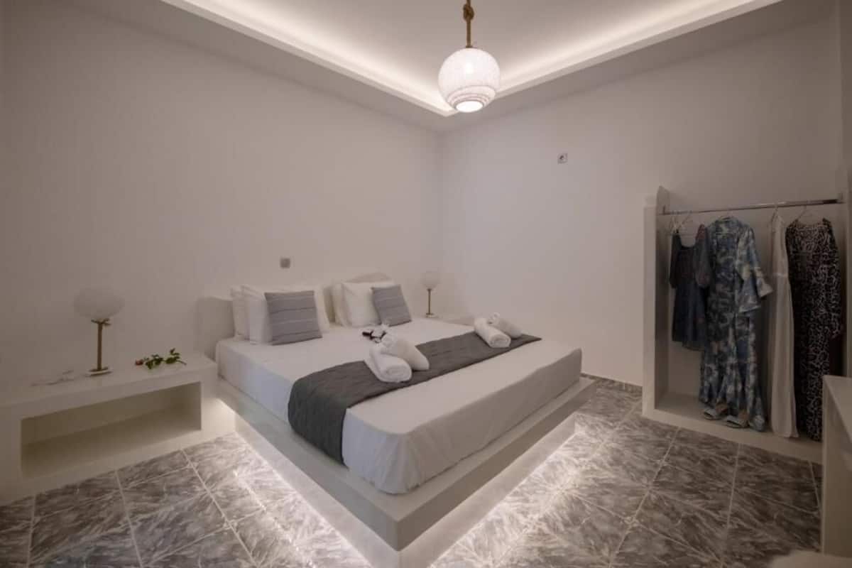 Un dormitorio moderno con cama, mesitas de noche, lámpara colgante y perchero.