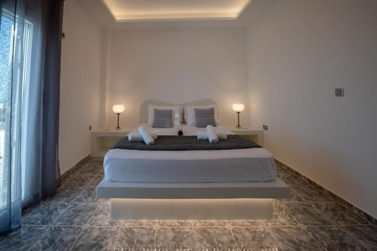 A modern hotel room with a large bed, bedside lamps, and a view through a window with curtains.