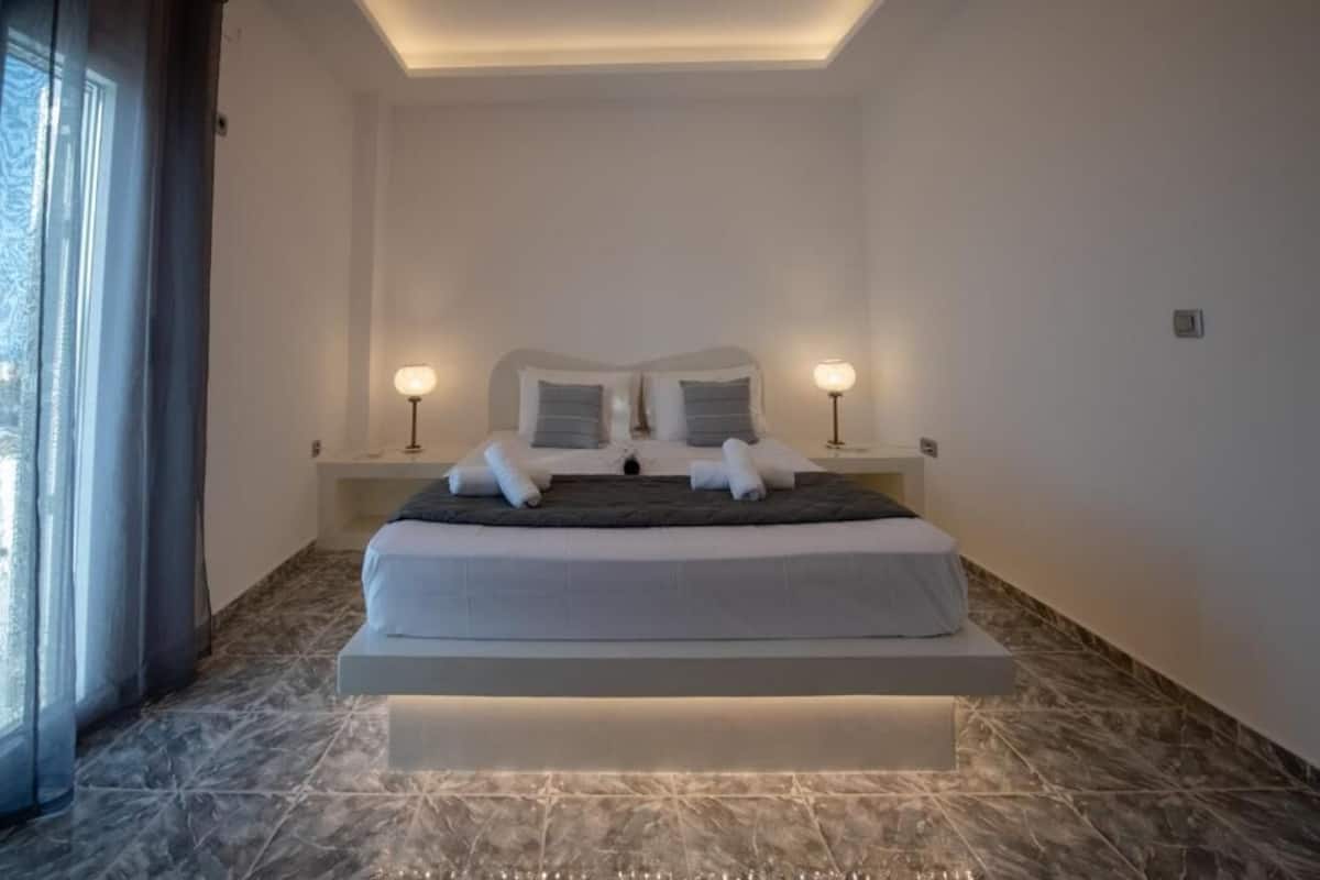Una habitación de hotel moderna con una cama grande, lámparas de noche y vistas a través de una ventana con cortinas.