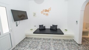 A room with a bed, a TV mounted on the wall, a small plant, and a decorative wall piece. - THE F SUITES (KARTERADOS)