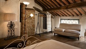 A rustic room with a bed, a sofa, a stone wall, a wooden ceiling, and a window. - Cottage with garden cave in the hills of Pietrasanta (Monteggiori)