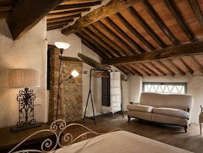 Une pièce rustique comprenant un lit, un canapé, un mur en pierre, un plafond en bois et une fenêtre.