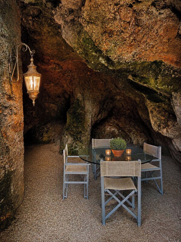 Un espace de restauration en plein air avec une table et des chaises, une lanterne suspendue et une paroi rocheuse en arrière-plan.