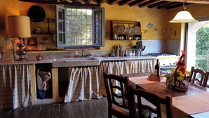 A rustic kitchen with a wooden table, a window with open shutters, and a hanging light fixture. - Cottage with garden cave in the hills of Pietrasanta (Monteggiori)