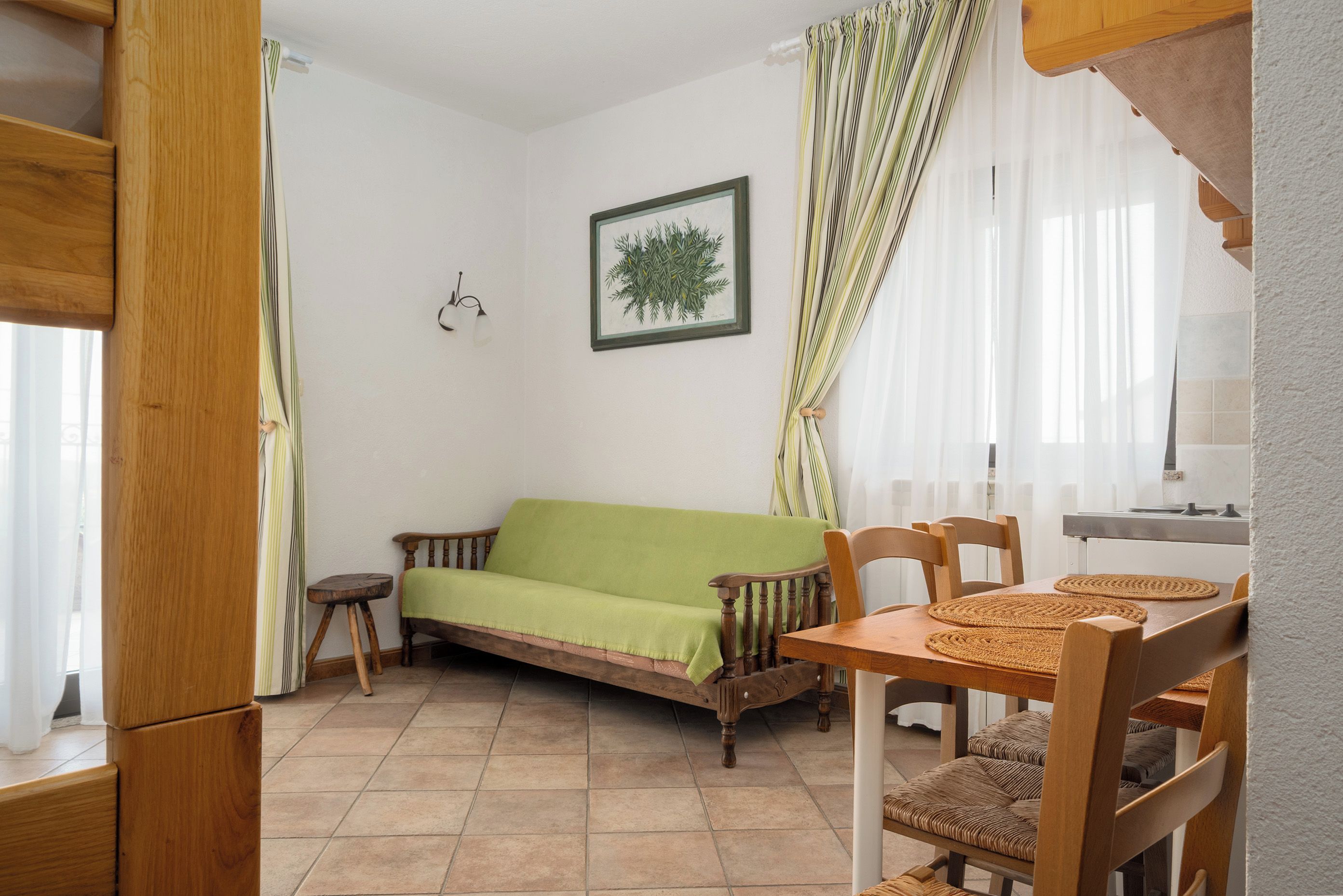 A cozy room with a wooden sofa, a small table, and a chair. There is a framed picture on the wall.