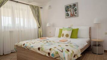 A bedroom with a bed, pillows, a bedside table, a lamp, a wall art piece, and a window with curtains.