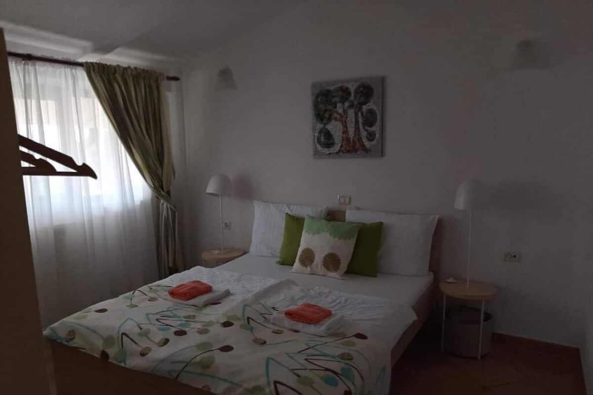 A bedroom with a bed, two bedside lamps, a painting on the wall, and a window with curtains.