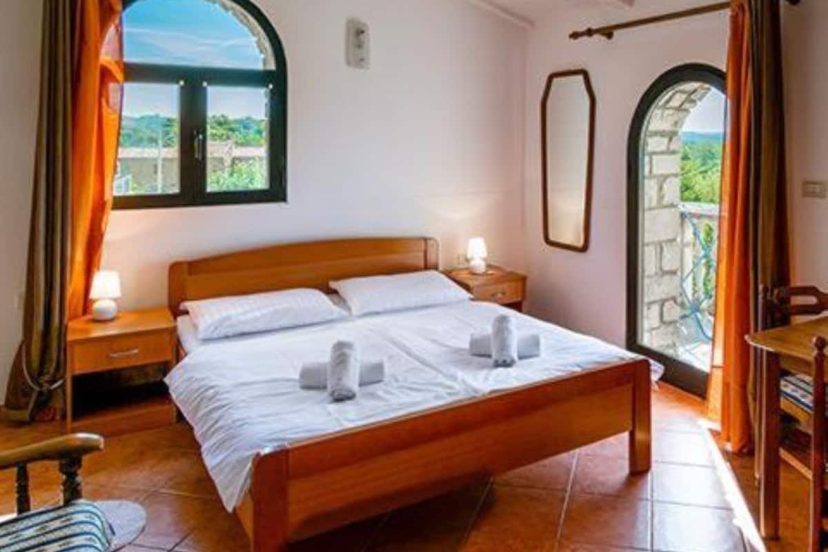 A bedroom with a wooden bed, two bedside tables, a window with curtains, and an arched doorway.