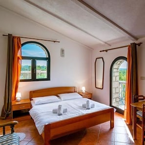 A bedroom with a wooden bed, two bedside tables, a window with curtains, and an arched doorway.