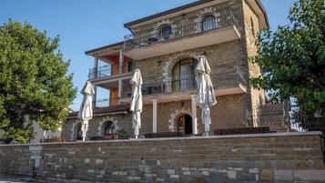 Un edificio de dos pisos con paredes de piedra, un balcón con barandilla de metal y asientos exteriores con sombrillas.
