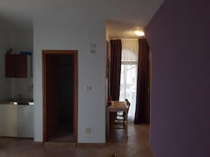 A room with a kitchen area, a dining table with chairs, and a door leading to another room.