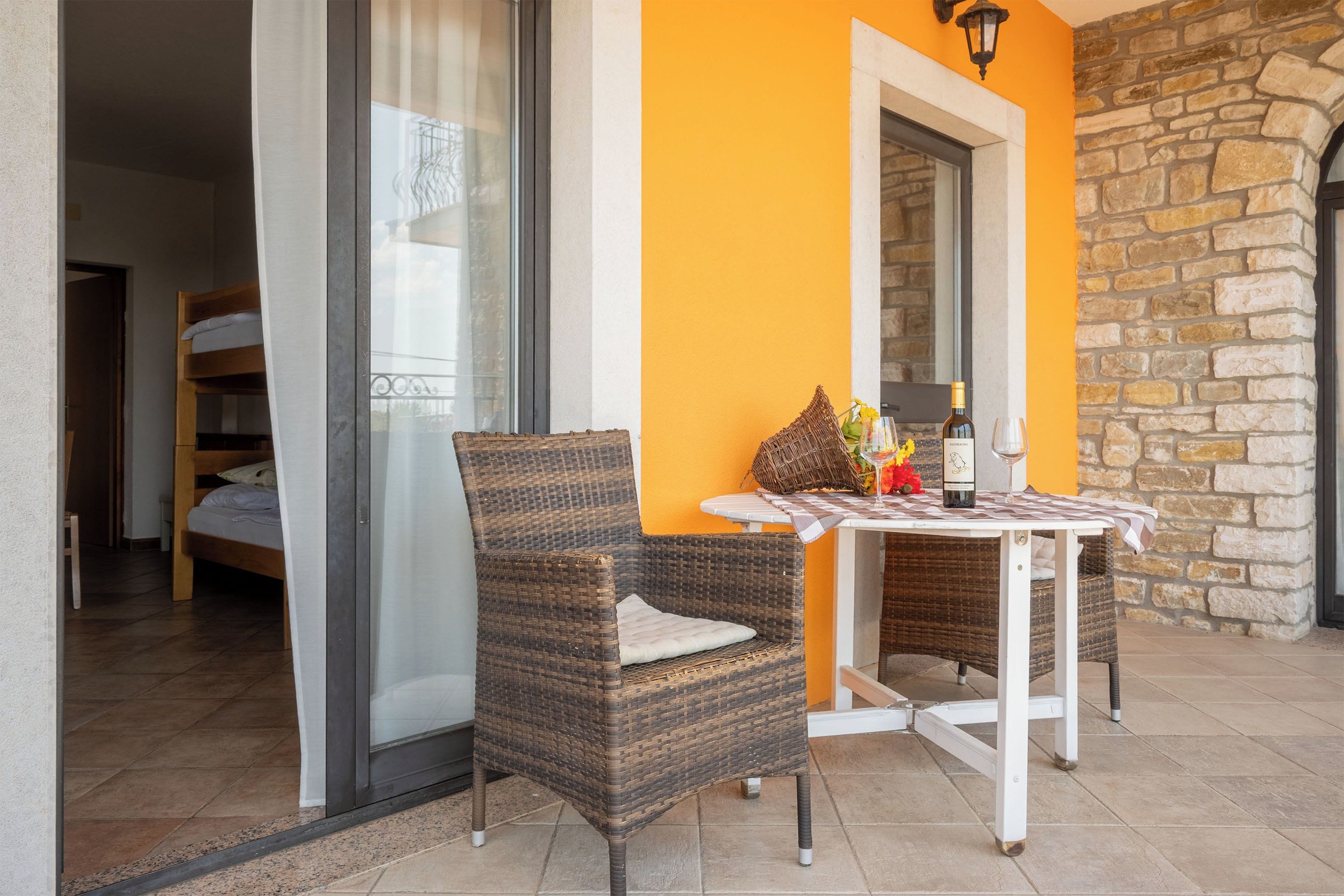 A balcony with wicker chairs, a table, and a bottle of wine.