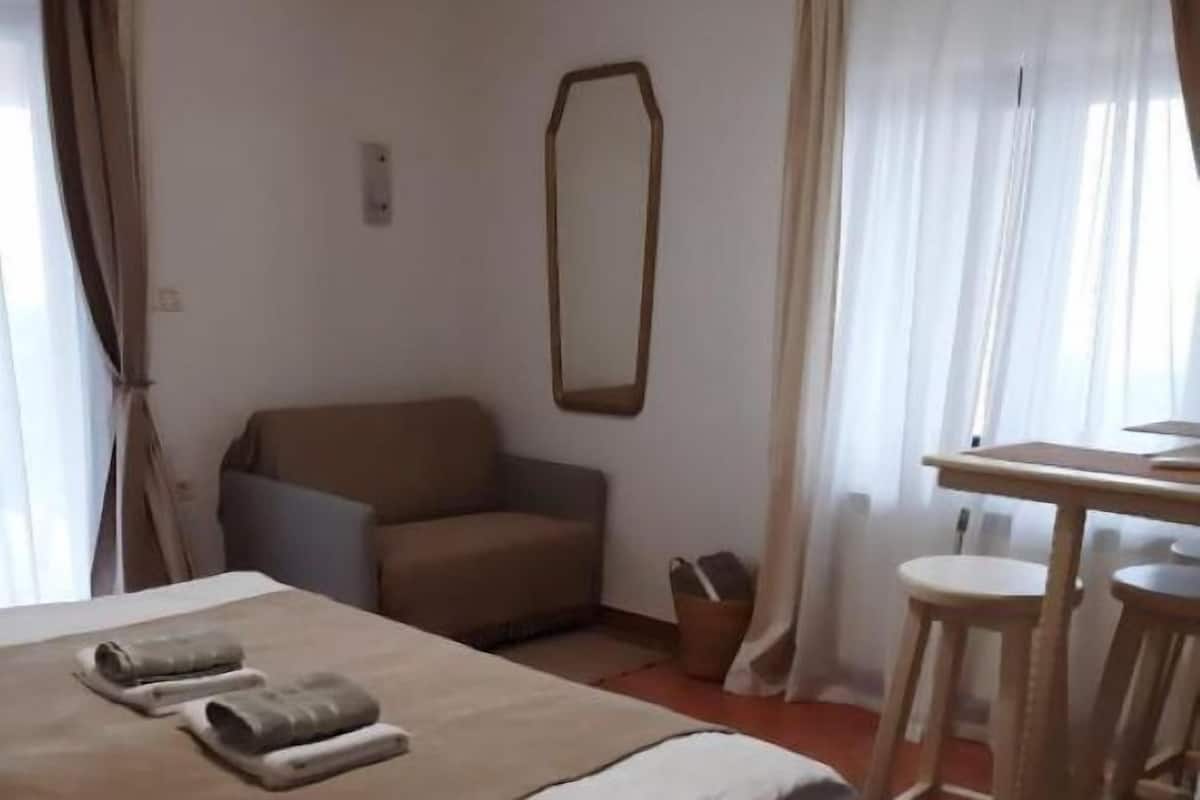 A bedroom with a bed, a chair, a table, and a mirror.