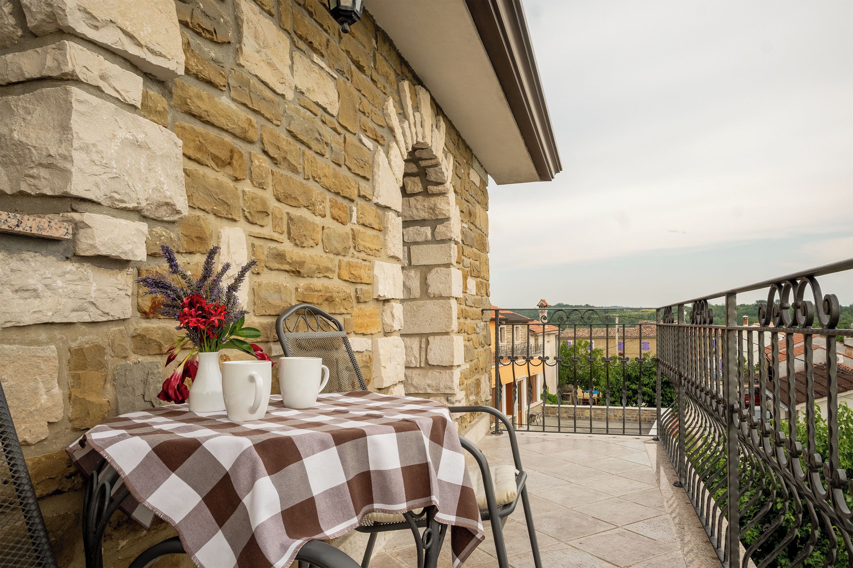 A balcony with a checkered tablecloth, a metal chair, and a vase of flowers.