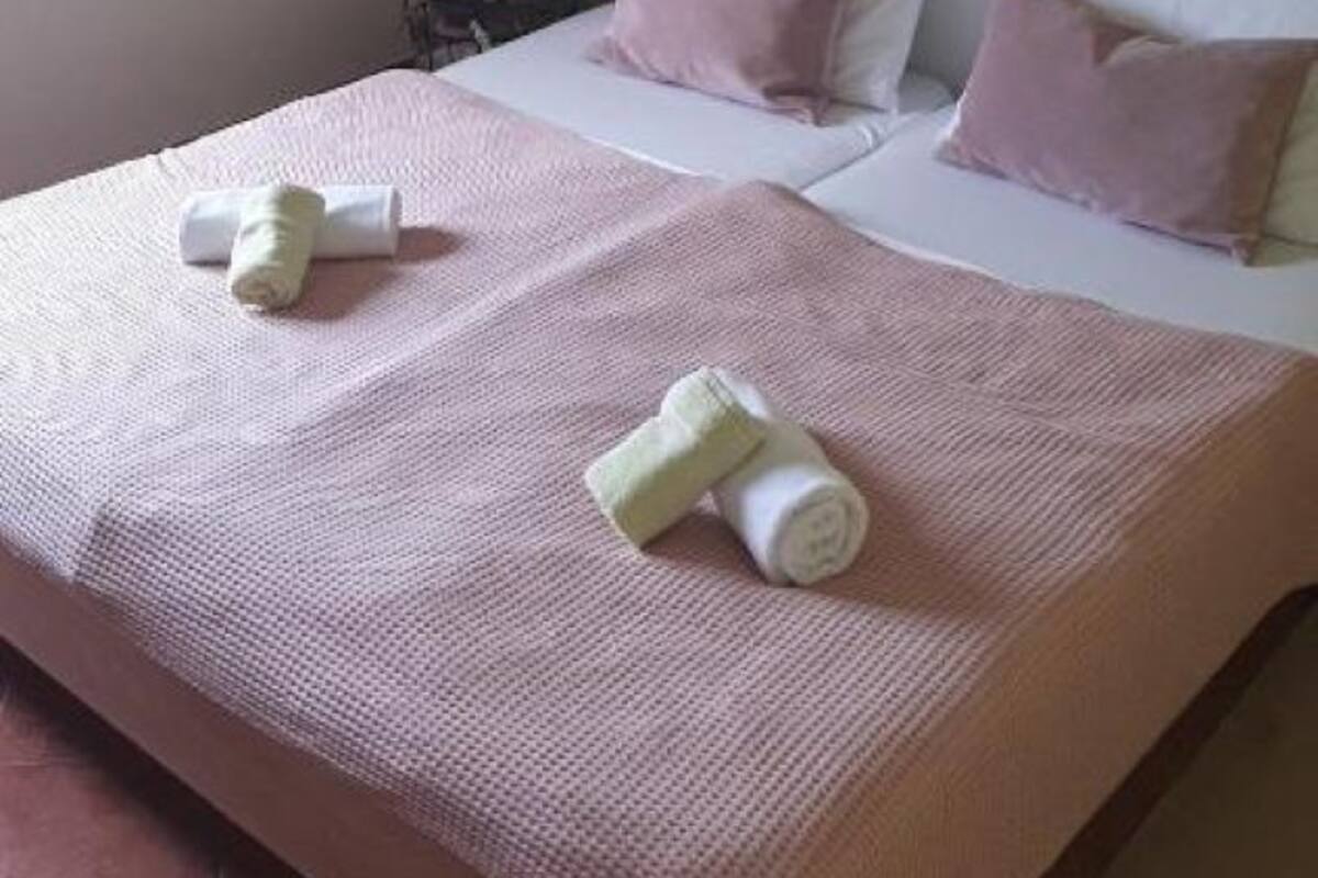 A double bed with two pillows, a bedside table, a mirror, and a painting on the wall.