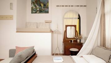 Un dormitorio con cama, mesita de noche, espejo, cuadro en la pared y ventana con cortinas.