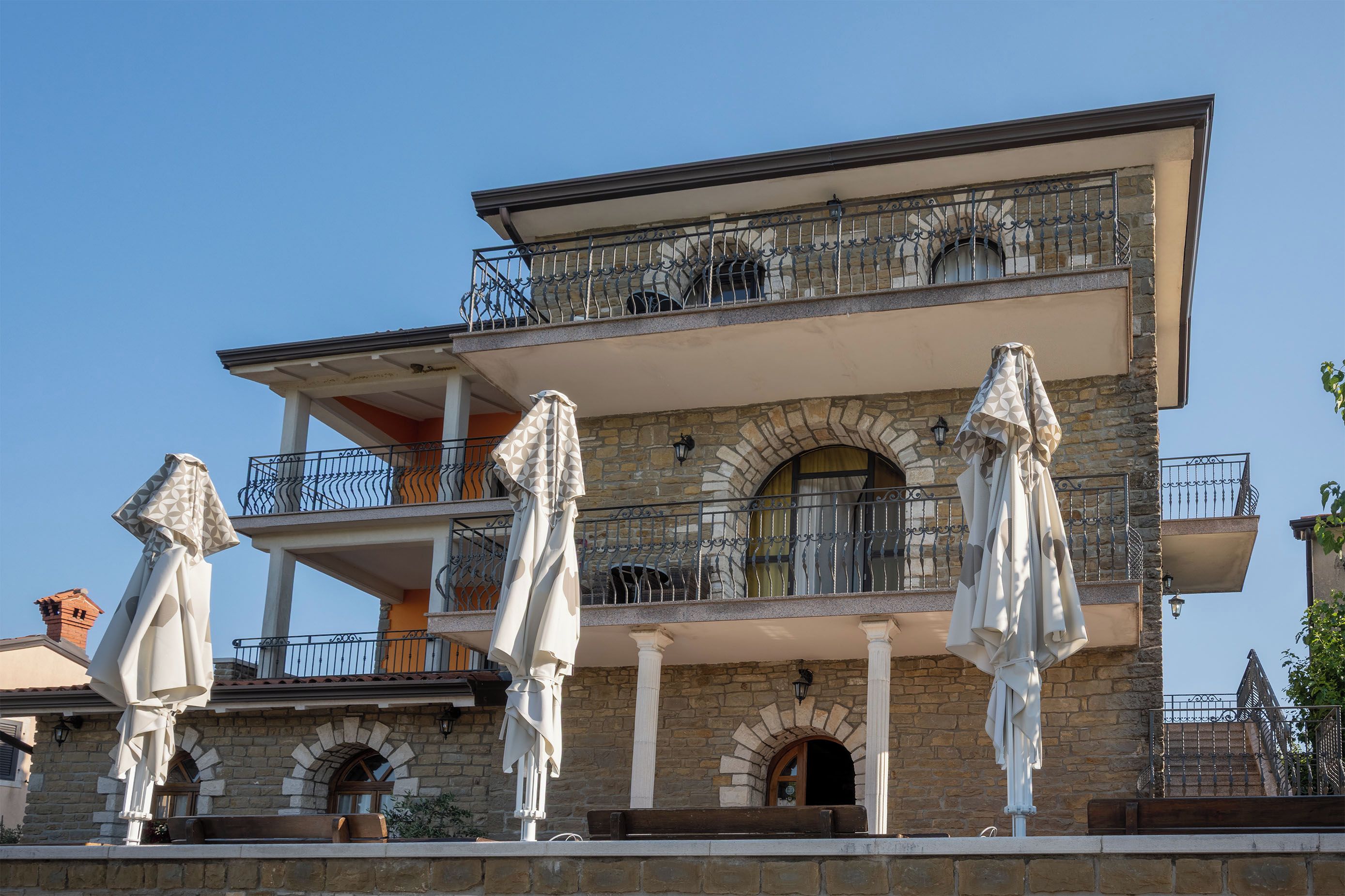 Un edifici de diverses plantes amb balcons, parets de pedra i paraigües exteriors.