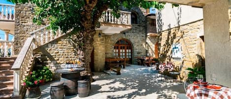 A courtyard with stone walls, a wooden staircase, and outdoor seating with checkered tablecloths.