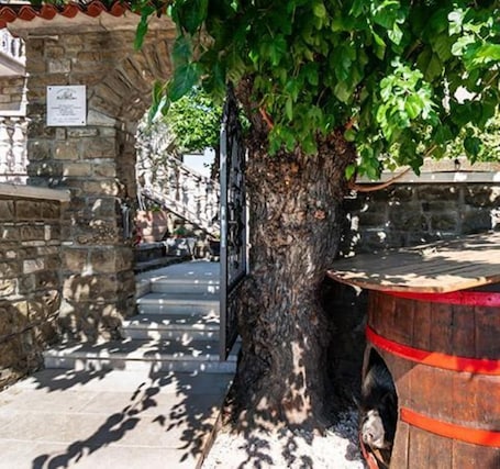 A stone building with a tree in front, a wooden barrel, and a staircase leading up.