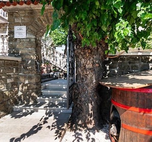A stone building with a tree in front, a wooden barrel, and a staircase leading up.
