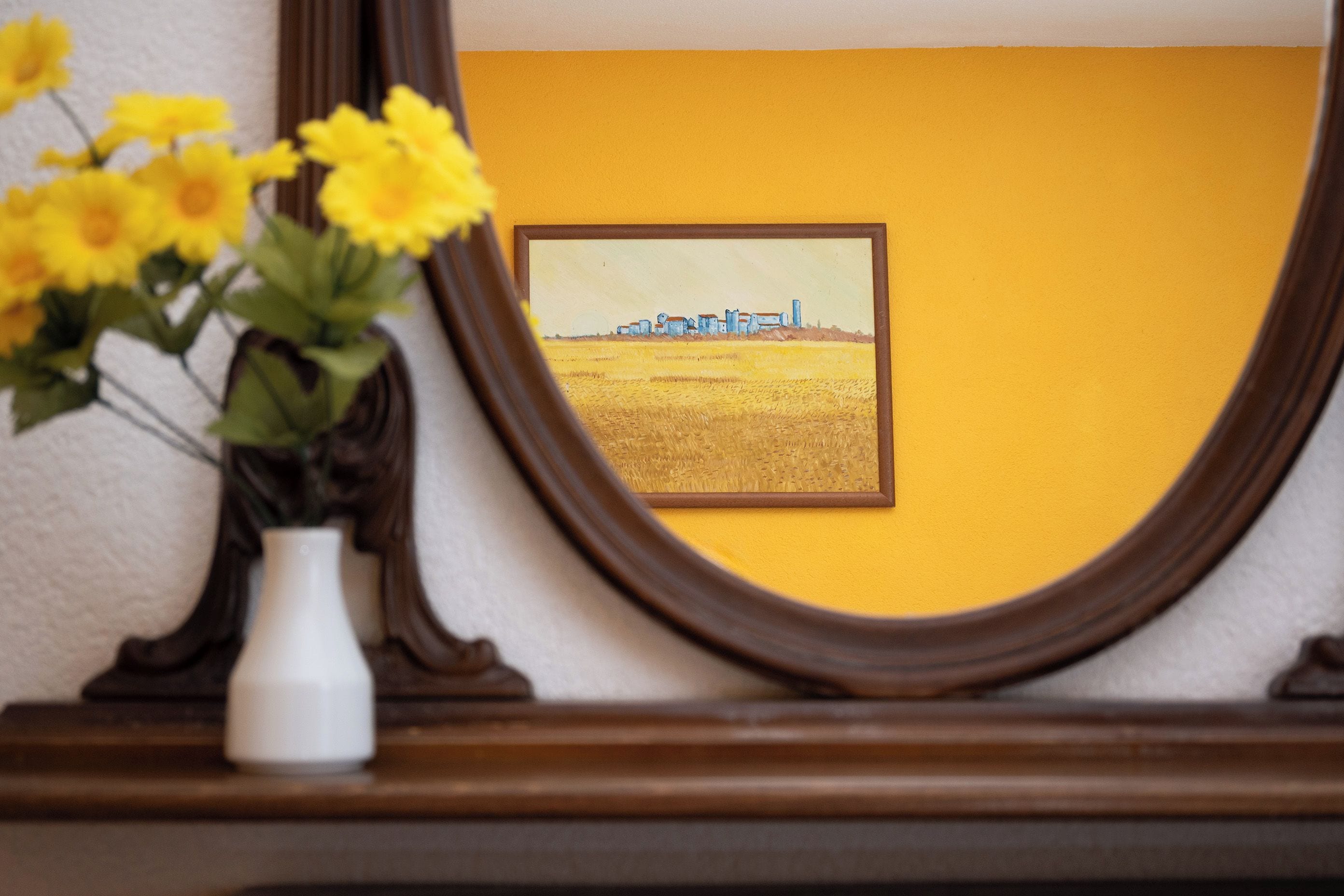 Une photographie encadrée représentant un paysage rural avec des bâtiments et un champ, accrochée à un mur dont le fond est jaune.