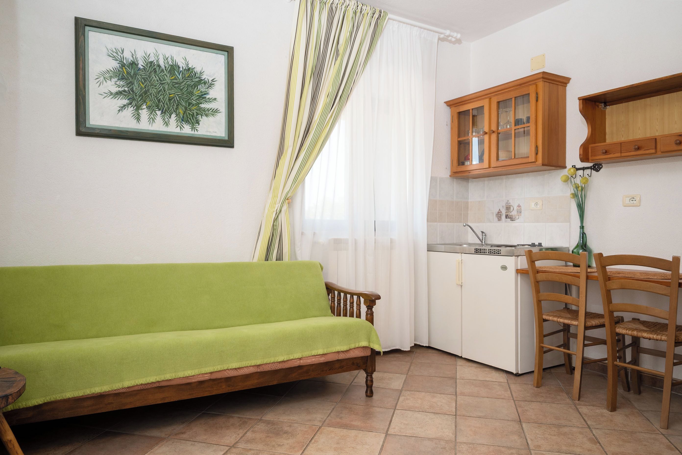 A compact living space with a sofa, a dining table with chairs, a kitchenette, and a window with curtains.