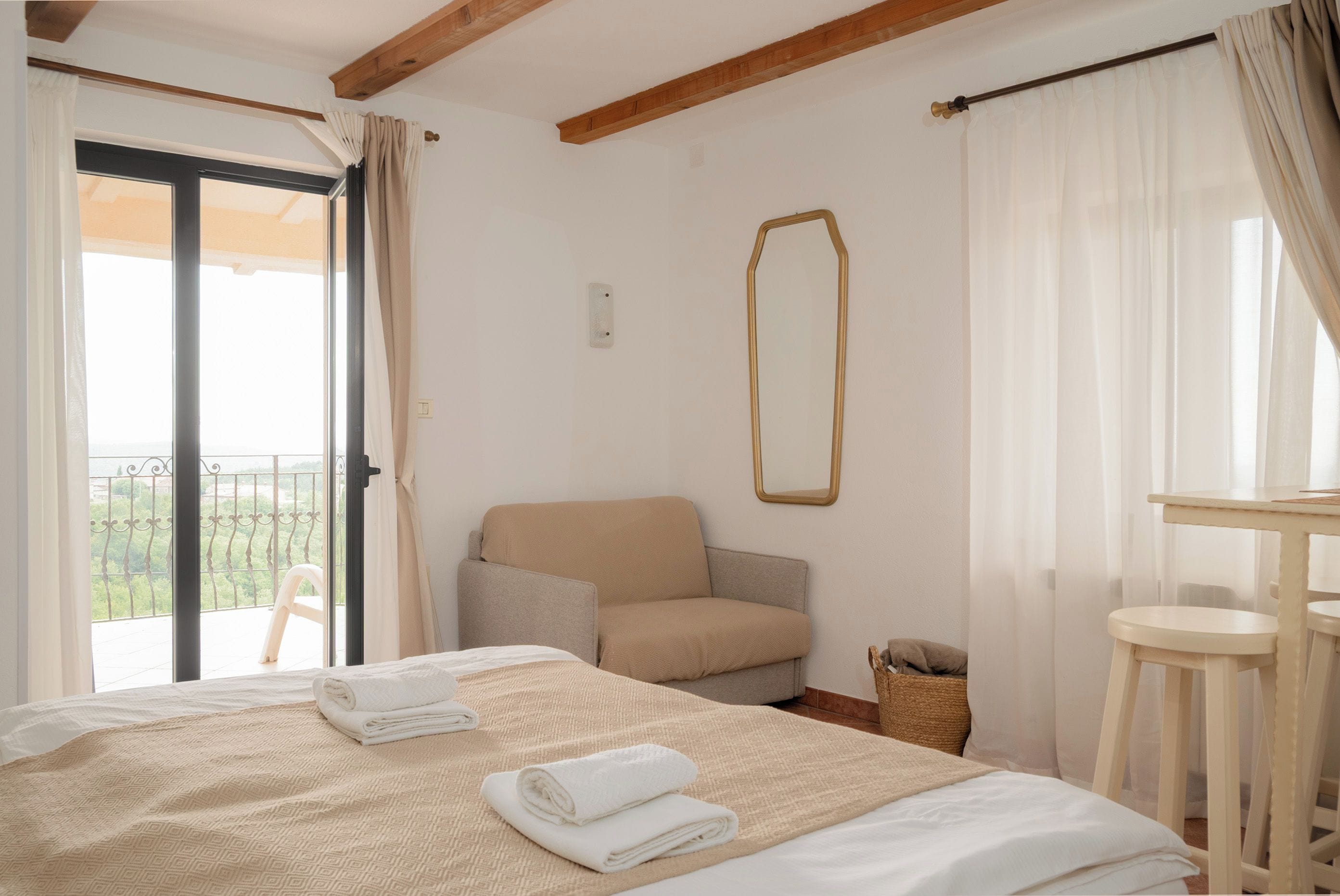 A bedroom with a bed, a chair, a table, and a balcony with a view.