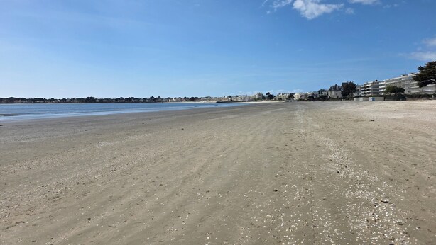 Ein weiter Sandstrand, bewölkter, klarblauer Himmel und Gebäude in der Ferne.