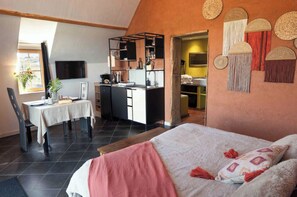 Un dormitorio con cama, una mesa de comedor con sillas, una kitchenette y un baño que se ve a través de una puerta abierta.