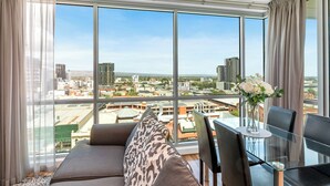 Een moderne kamer met grote ramen, een bank, een glazen tafel en een bloemenvaas.