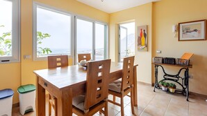 A dining area with a wooden table and chairs, large windows, a waste bin, and a small table with baskets and plants. - Family villa Green House - Private pool - Garden - Tenerife North Bajamar (Bajamar)