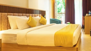 A hotel room with a large bed, a wooden headboard, and a view of greenery outside.