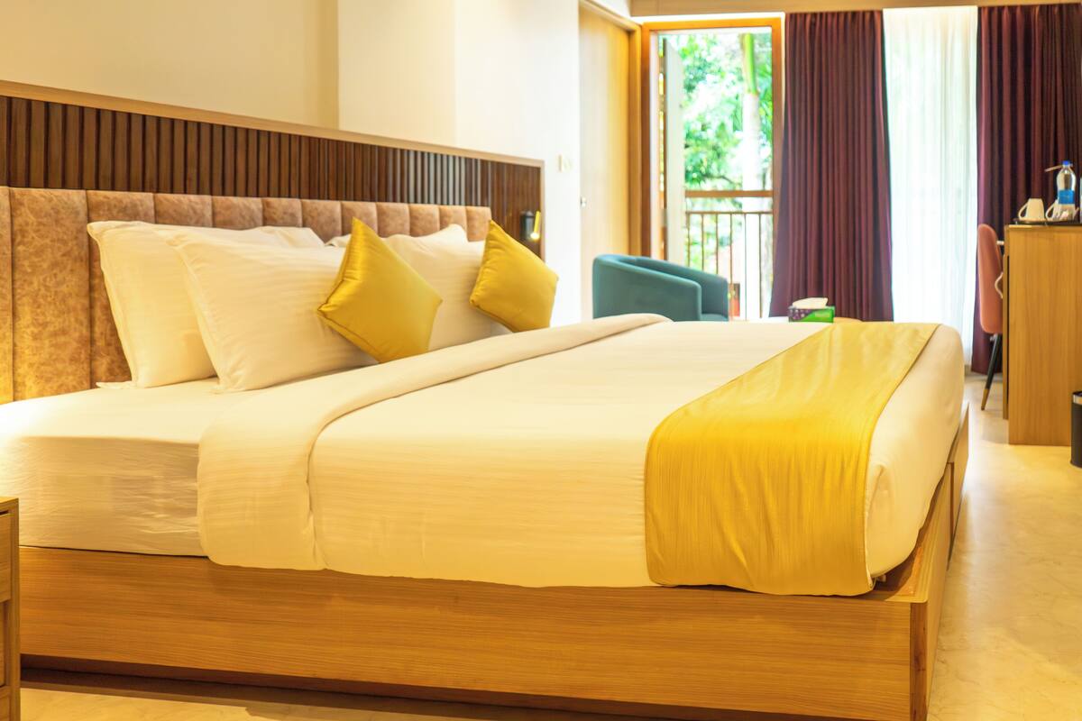 Habitación de hotel con una cama grande, cabecera de madera y vistas a zonas verdes.