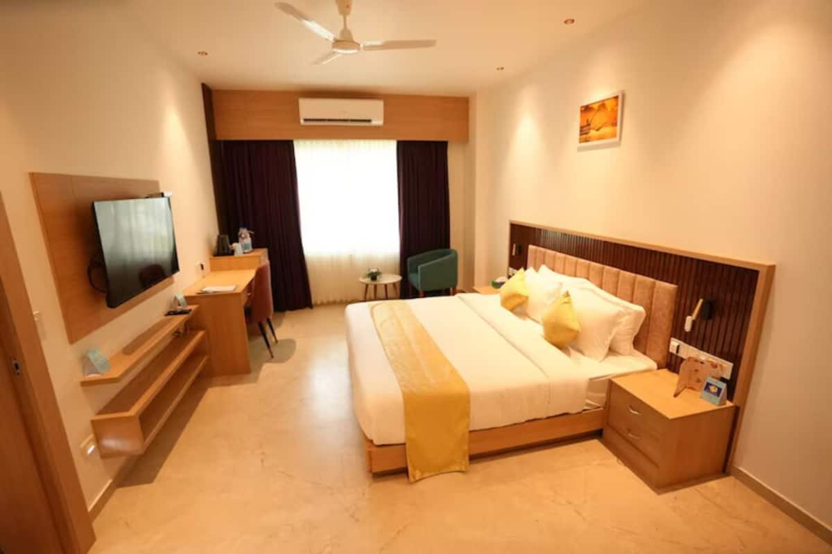 Habitación de hotel con cama, mesita de noche, escritorio, silla, televisor y aire acondicionado.