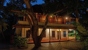 A two-story building with a balcony, large trees, and a well-lit entrance.