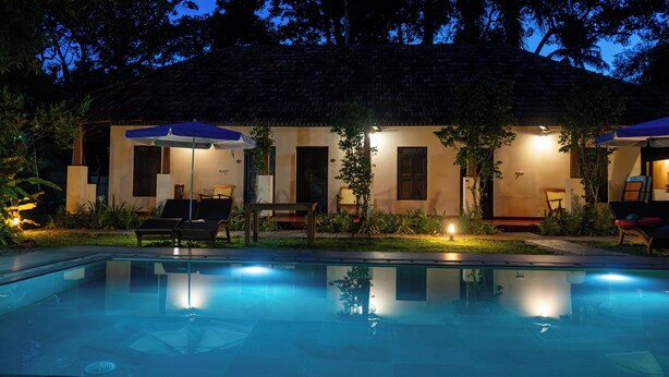 A poolside area with lounge chairs, umbrellas, and a building with a tiled roof.