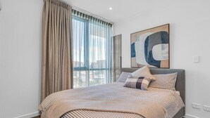 A bedroom with a bed, a large window with curtains, a city view, and a piece of abstract art on the wall. - Adelaide Central Skyline Panoramic Suite One (Adelaide)