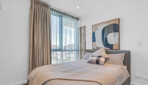 A bedroom with a bed, a large window with curtains, a city view, and a piece of abstract art on the wall. - Adelaide Central Skyline Panoramic Suite Four (Adelaide)