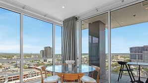 A high-rise room with a glass table and chairs, large windows, and a city view. - Adelaide Central Skyline Panoramic Suite One (Adelaide)
