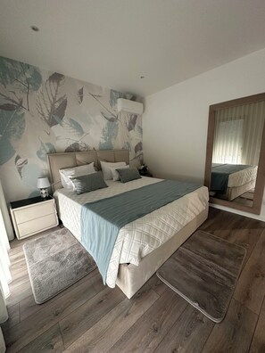 Une chambre à coucher comprenant un lit, des tables de chevet, un miroir et un mur orné d’un motif de feuilles.