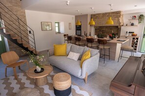 Ein modernes Wohnzimmer mit Sofa, Couchtisch und Essbereich mit Stühlen, im Hintergrund eine Küche.