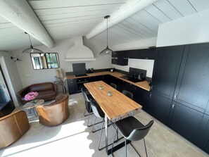 Une cuisine moderne avec une table Ă manger en bois, des meubles de rangement noirs et des luminaires suspendus.