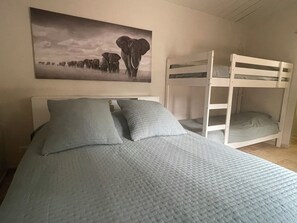 Un lit superposĂ© avec une tĂȘte de lit blanche, deux oreillers et un tableau reprĂ©sentant des Ă©lĂ©phants, accrochĂ© au mur.