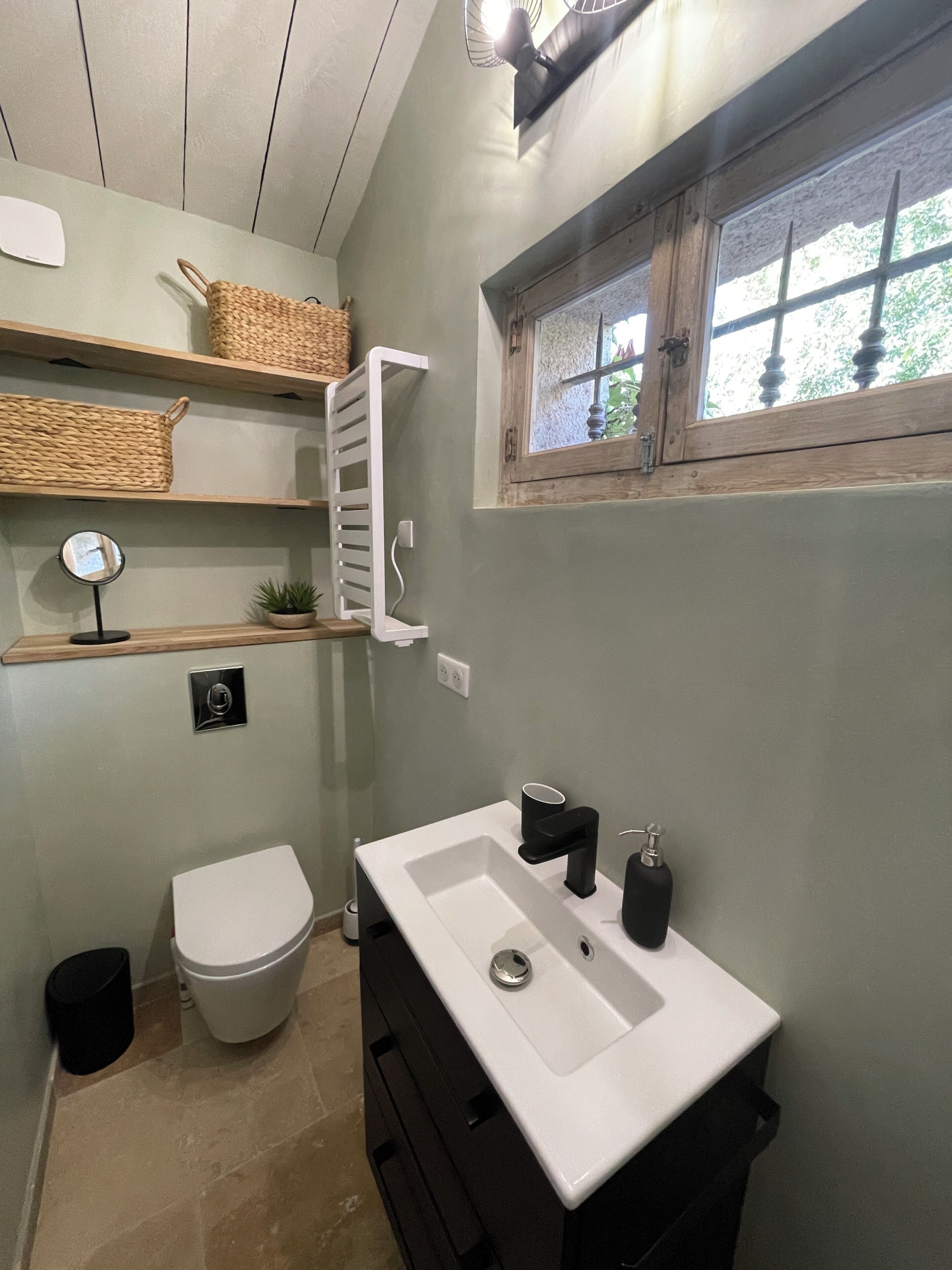 Casa de banho com lavatório branco, armário preto e janela com vista para vegetação.