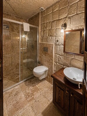 A bathroom with a stone wall, a glass-enclosed shower, a toilet, and a wooden vanity with a sink.