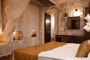 A bedroom with stone walls, a bed with a brown bedspread, a wooden nightstand, and a mirror.