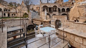 A rooftop terrace with stone walls, a white table with chairs, and a view of historic buildings.