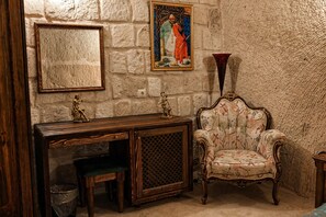 A room with a stone wall, a wooden console table with a chair, a framed picture, and a vase.