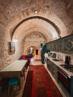 A kitchen with stone walls, an arched ceiling, a central island, and a red patterned rug.